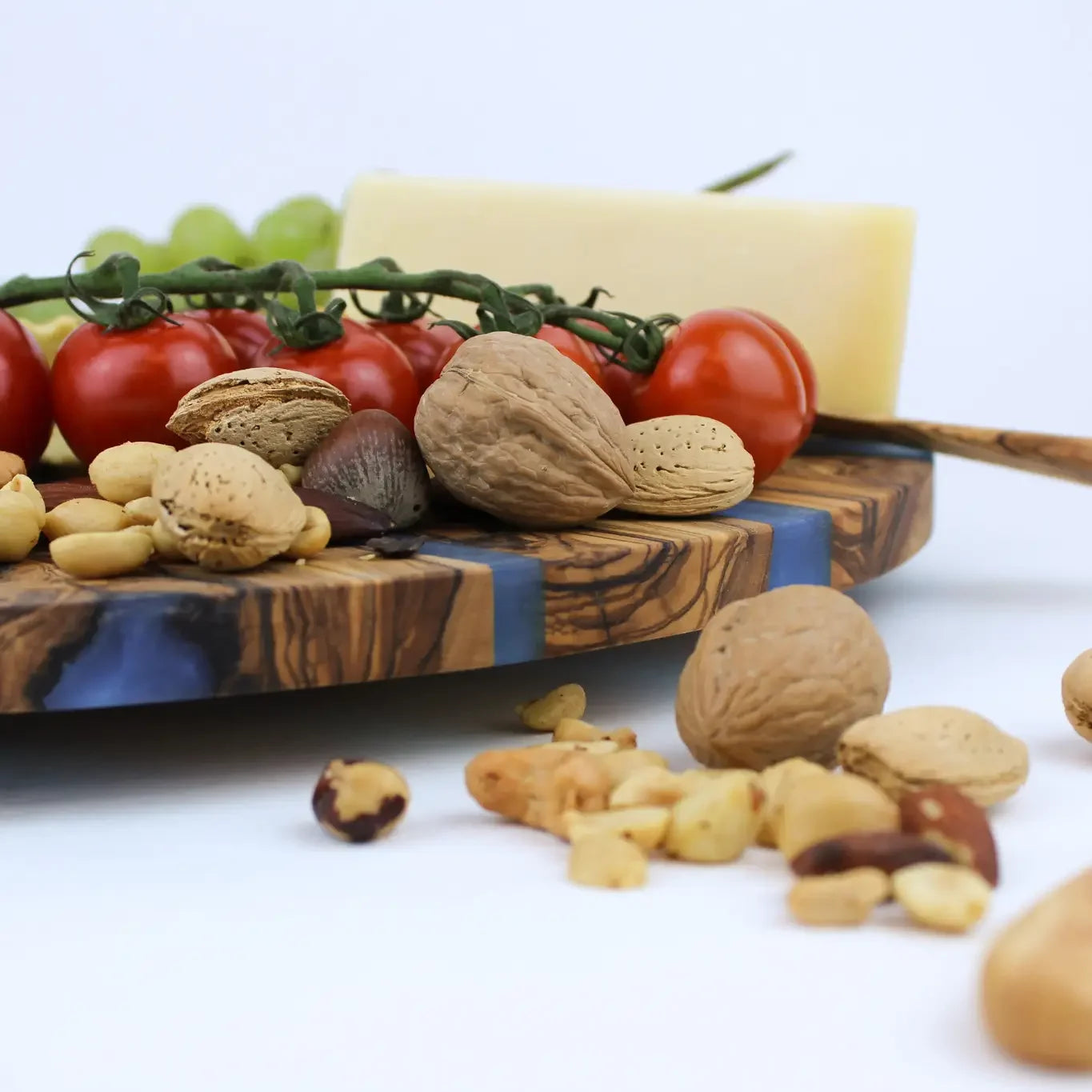 Assorted nuts, tomatoes, and cheese on a wooden lazy susan board with a white background