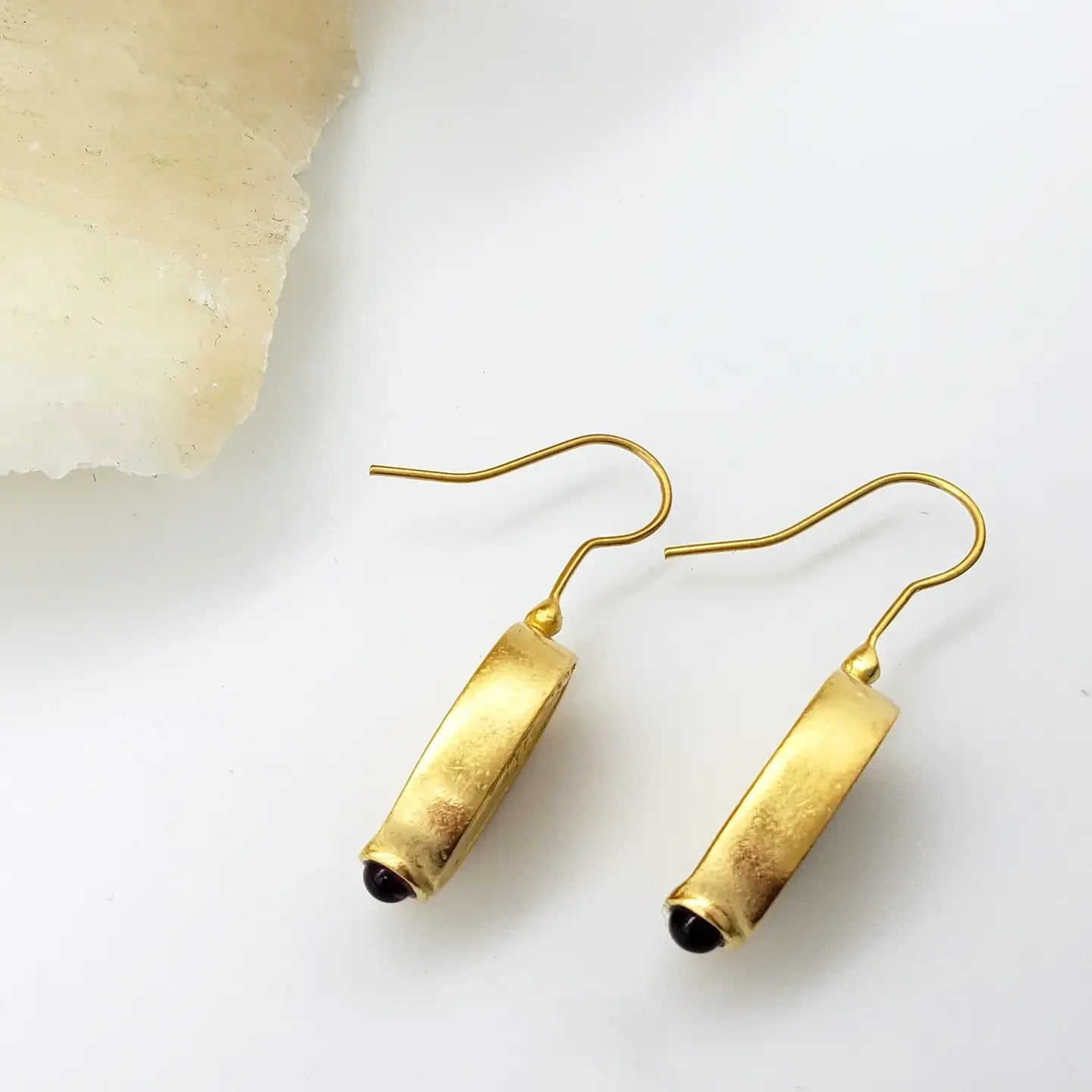 Aphrodite gold earrings on their side on a white background near parchment
