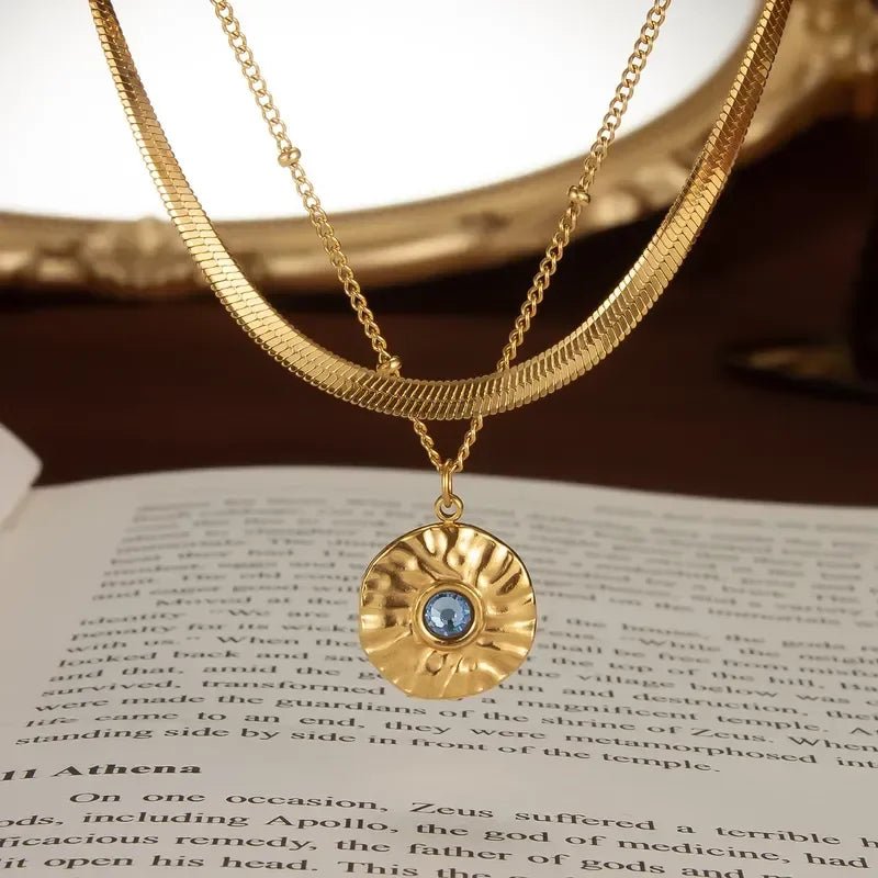 Two layer gold necklace with a blue gemstone pendant over an open book