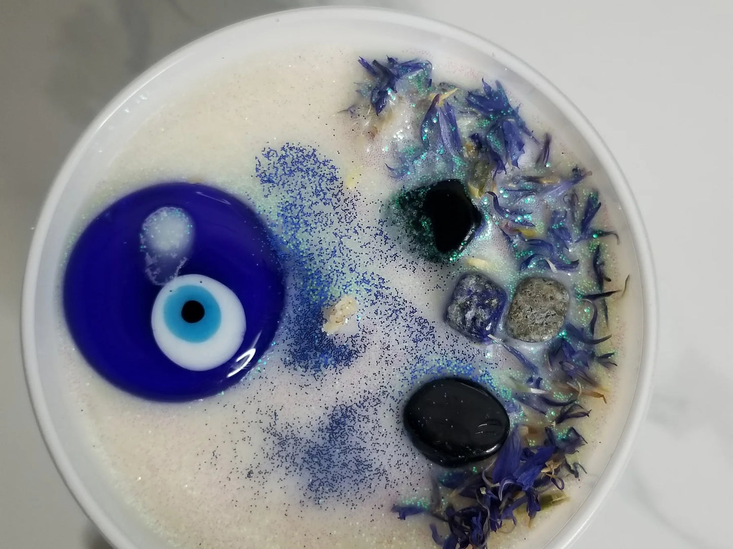 Top of candle with blue eye decoration and dried flowers on a white background