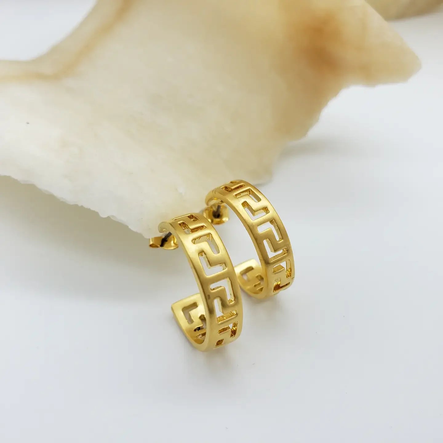 Gold hoop earrings with a Greek key design on a light background