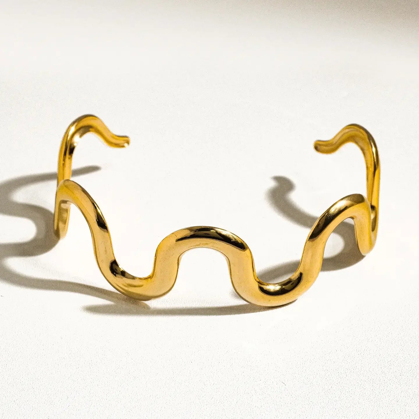 Gold bracelet with wavy design on a light background