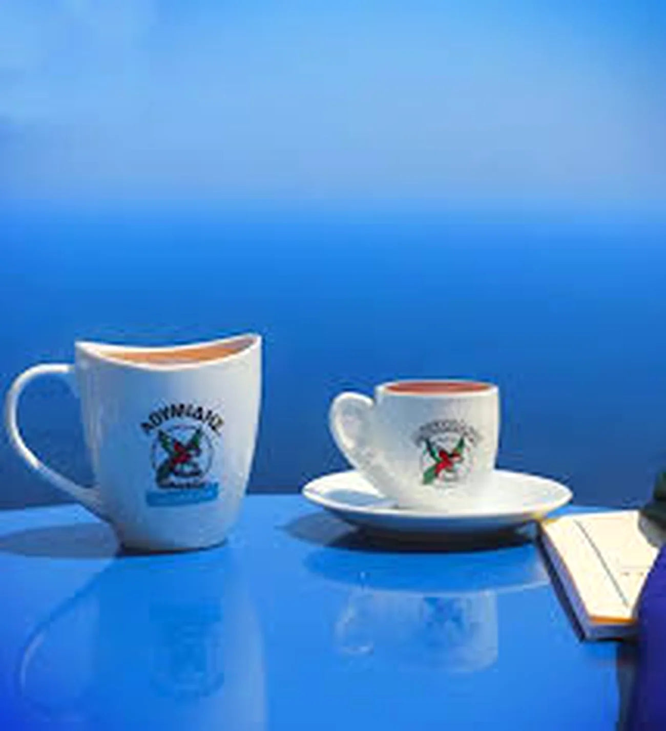 Two white ceramic cups with handles on a blue surface