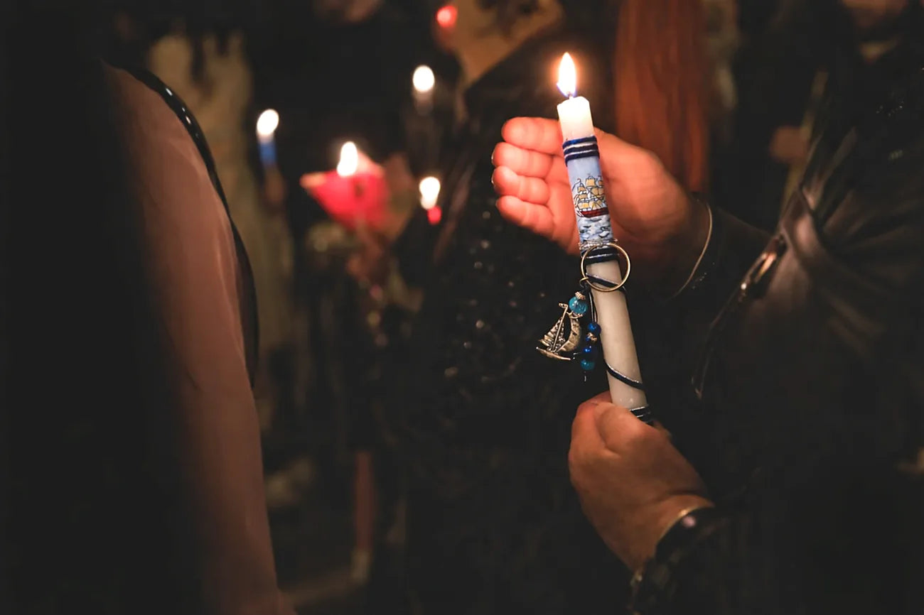 Hand holding a lit candle with decorative elements in a dimly lit setting