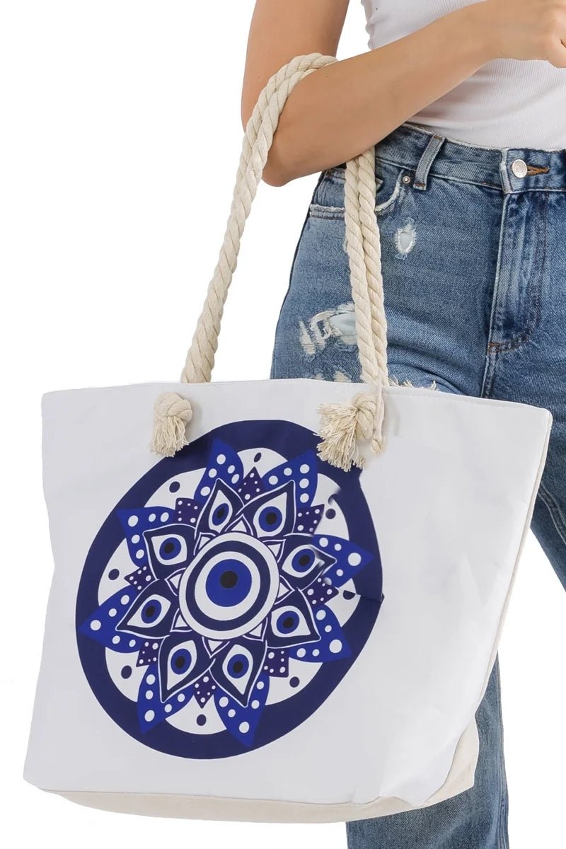 White tote bag with blue evil eye mandala design held by a person wearing jeans