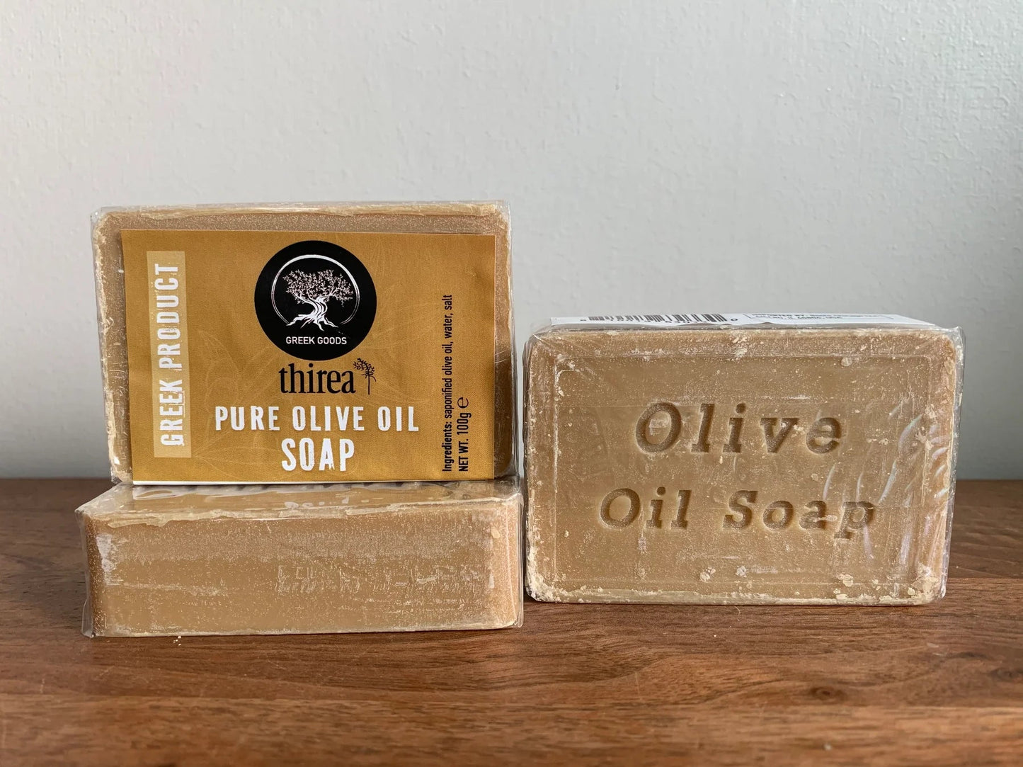 Three bars of olive oil soap with packaging on a wooden surface