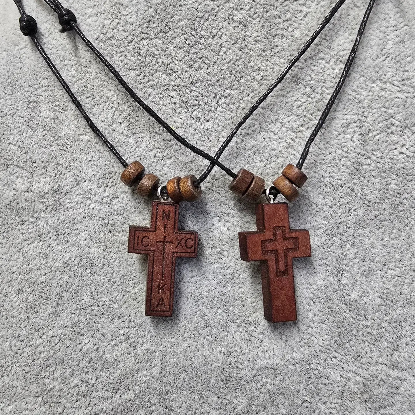 Two wooden cross necklaces with beads on a textured surface