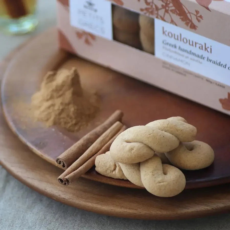 Koulouraki cookies on a wooden plate with cinnamon sticks and a box in the background.