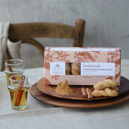 Box of koulouraki cookies on a table with glasses of honey and cinnamon sticks
