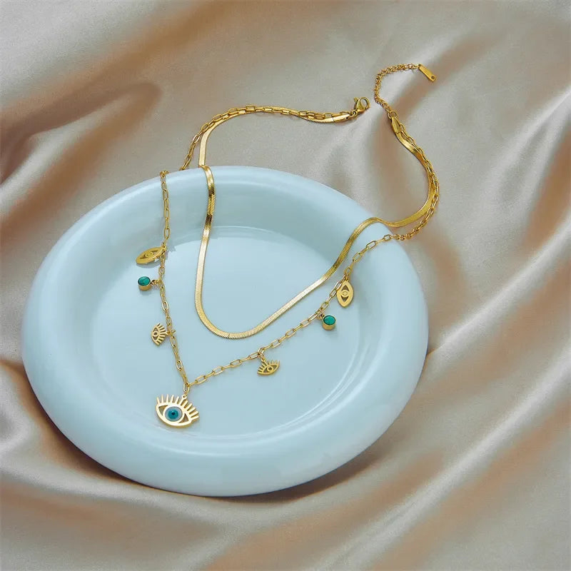 Gold jewelry set with double layer necklace on a light blue dish against a beige fabric background