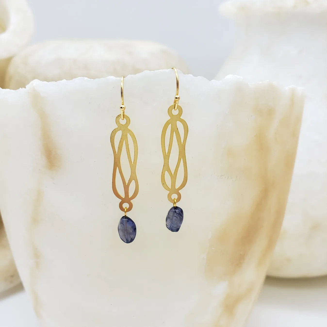Gold earrings with dark gemstones on a soft white fabric background
