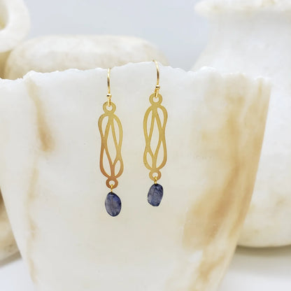 Gold earrings with dark gemstones on a soft white fabric background
