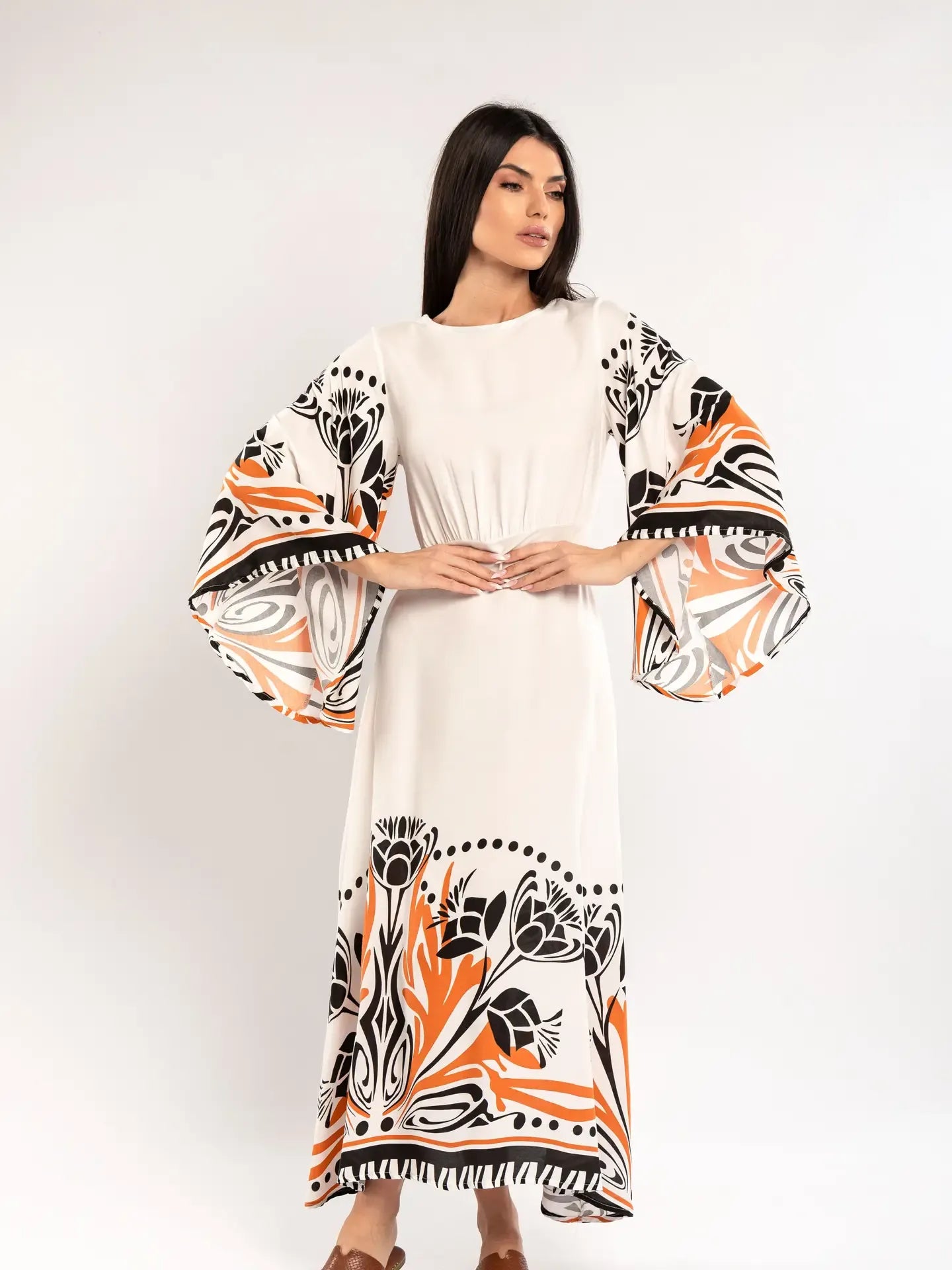 Woman wearing a white dress with black and orange floral patterns on a plain background