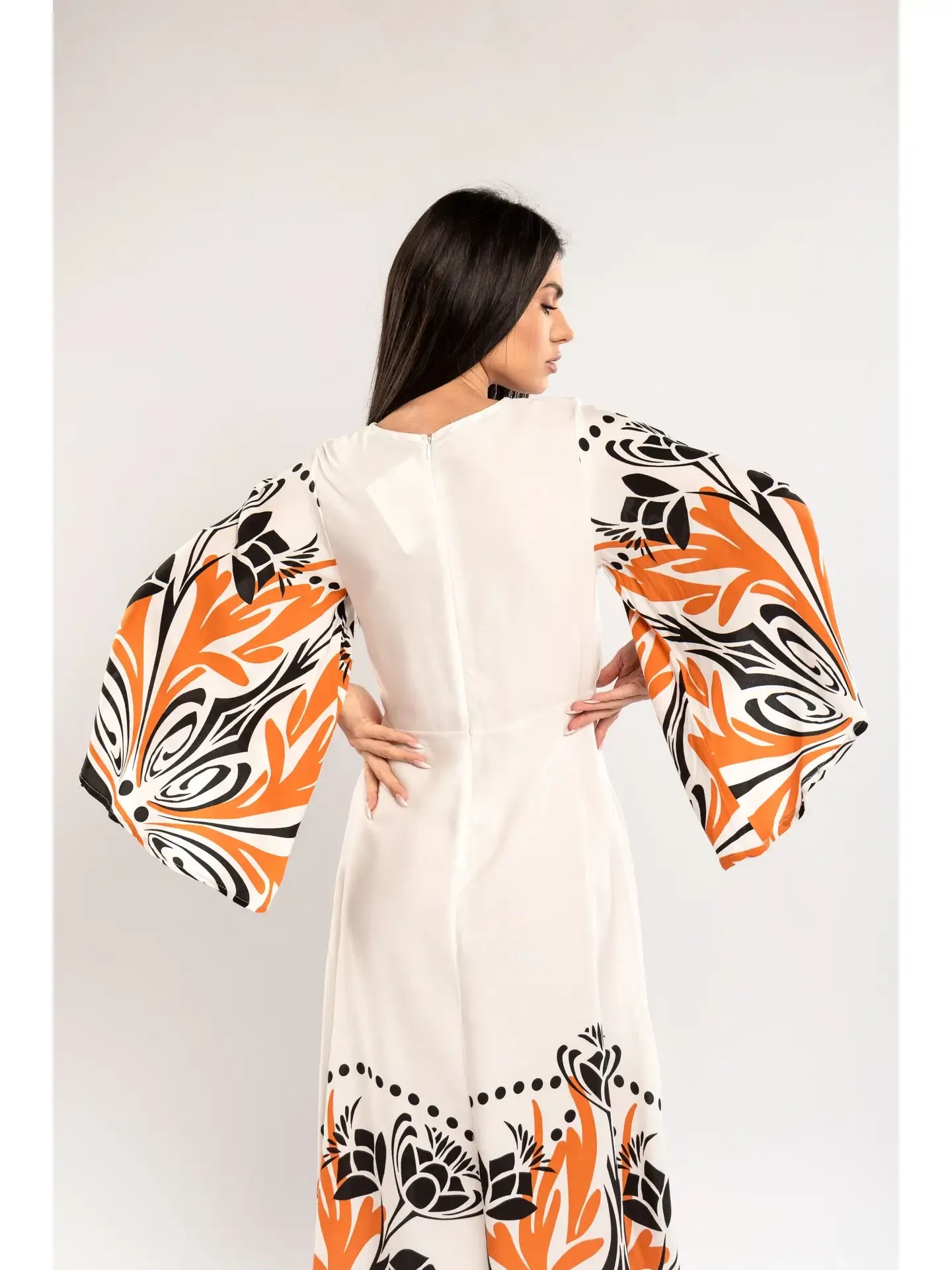 Woman wearing a white dress with orange and black floral patterns on a plain background