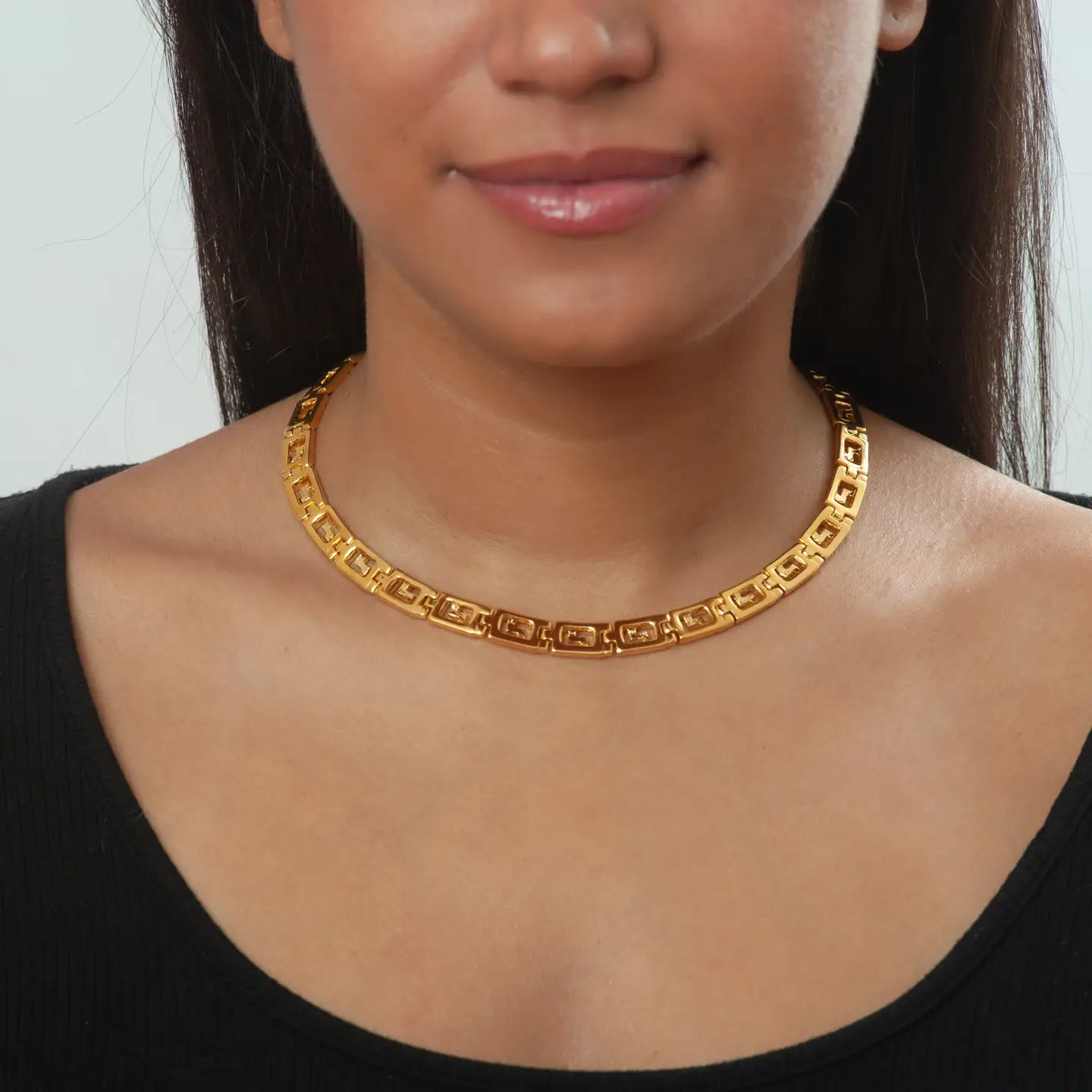 Gold necklace with intricate Greek Key Meander design worn by a person against a neutral background