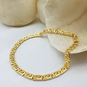 Gold necklace with intricate Greek Key Meander design on a white surface