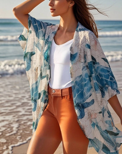 Woman on a beach wearing a sea turtle cover-up and white top with orange pants.