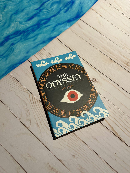 Book titled 'The Odyssey' by Homer on a wooden surface with a blue fabric in the background