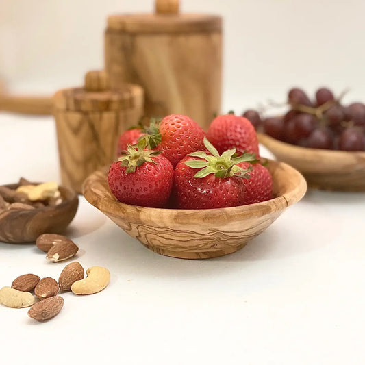 Wooden bowl with strawberries on a white surface with nuts and grapes in the background