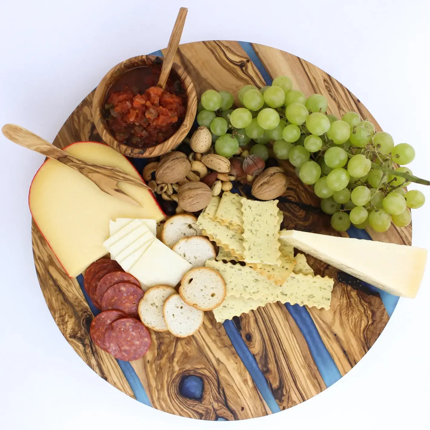Wooden lazy susan charcuterie board with assorted cheeses, meats, crackers, and grapes on a white background