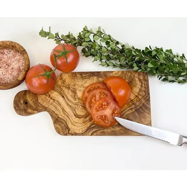 Wooden cutting board with sliced tomatoes, a knife, and herbs on a white background