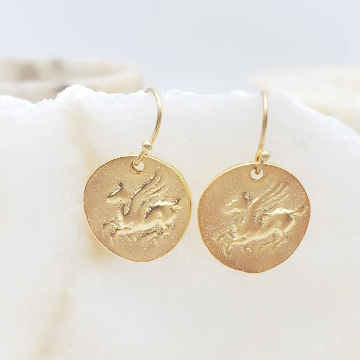 Gold Pegasus earrings with engraved designs on a white surface