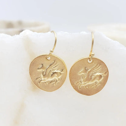 Gold Pegasus earrings with engraved designs on a white surface