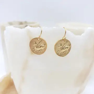 Gold Pegasus earrings on a white shell with a light gray background