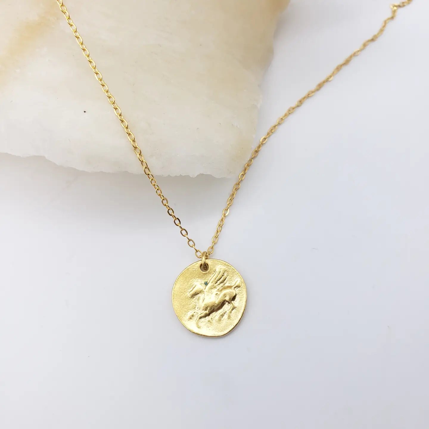 Gold necklace with a round Pegasus pendant on a light background