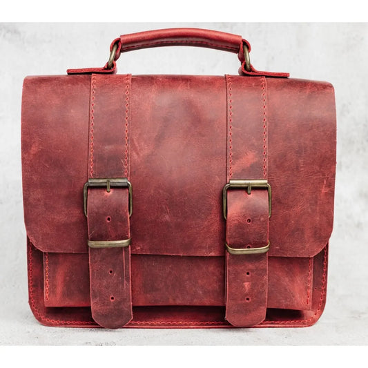 Red leather satchel with brass buckles on a light gray background