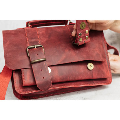 Red leather satchel bag with gold buckles held by a hand on a light background