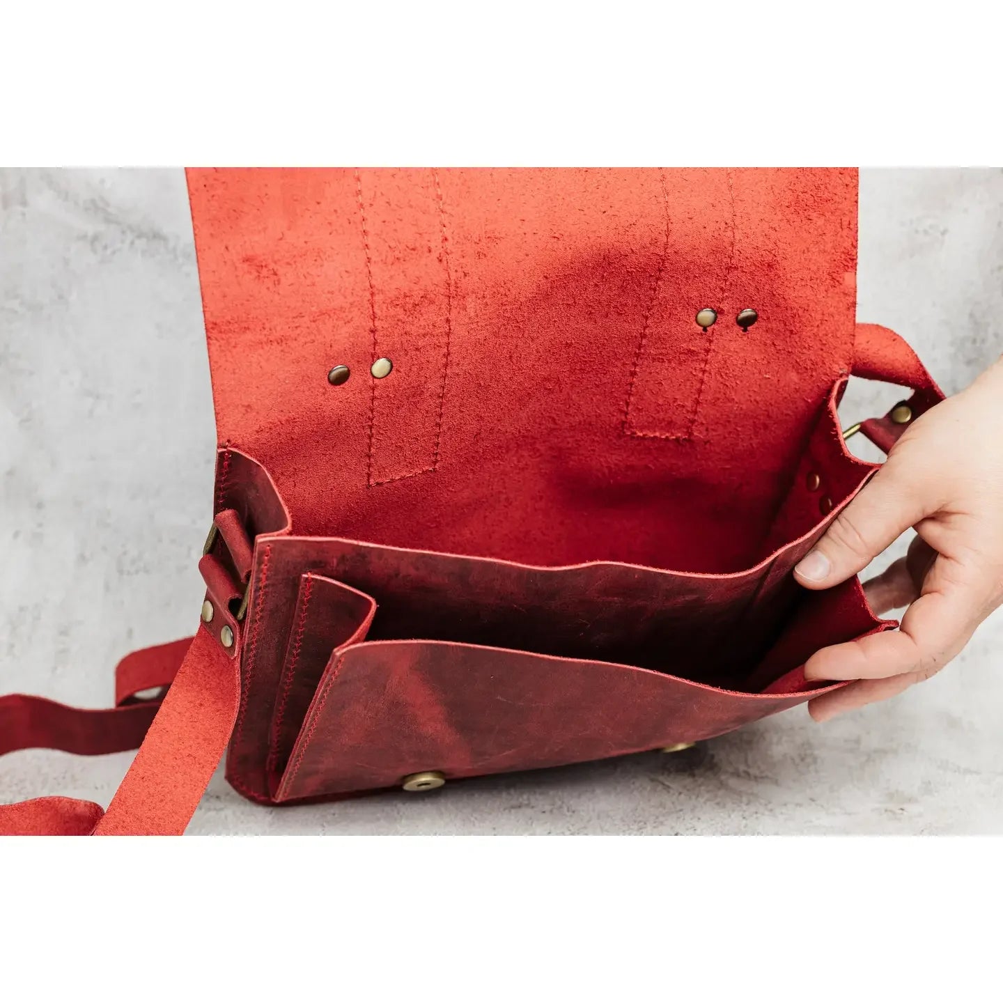 Red leather bag with a hand opening it on a light gray background