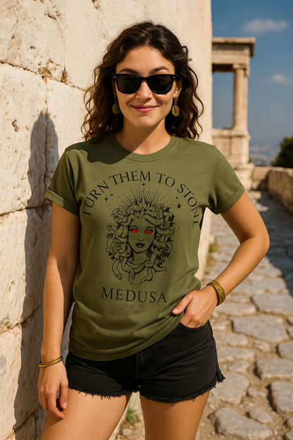 Woman wearing a green t-shirt with Medusa graphic and the text "TURN THEM TO STONE", standing in front of ancient ruins