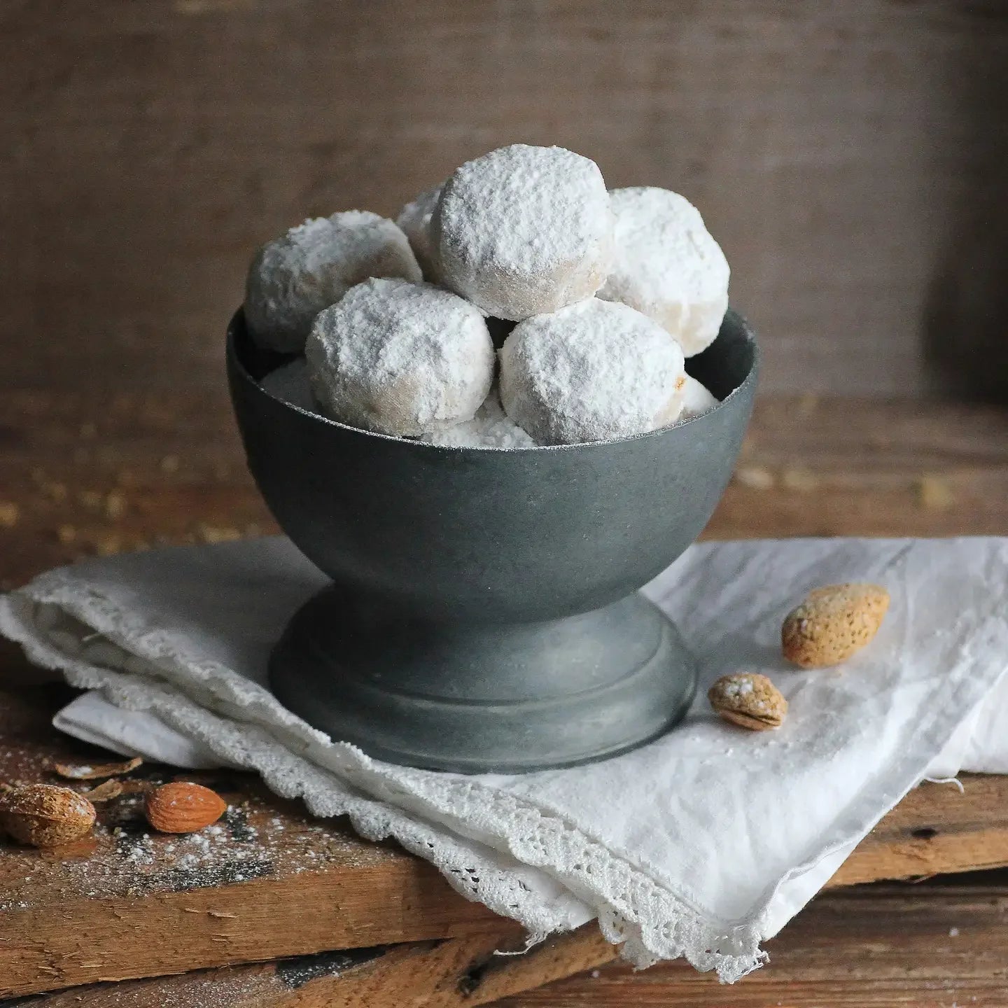 Bowl of powdered sugar cookies on a rustic wooden table with almonds
