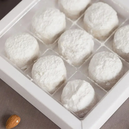 White powdered sugar Greek Kourabies in a clear plastic container on a gray surface