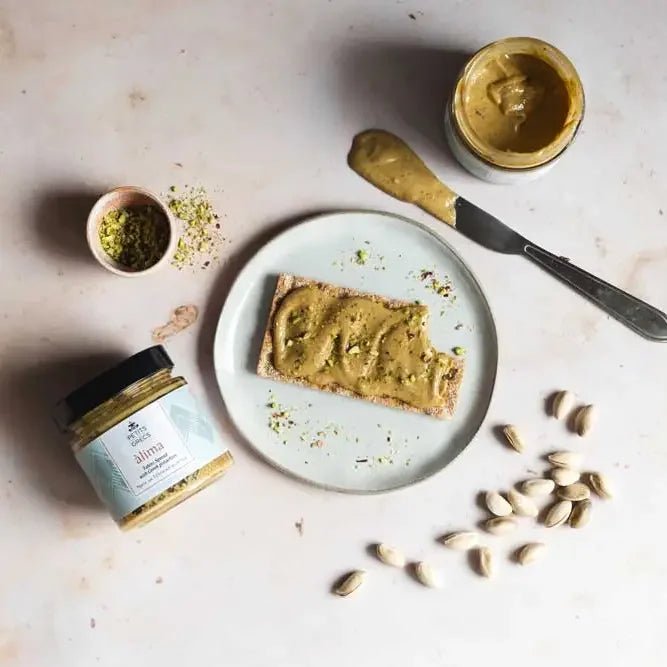 Pistachio tahini spread on toast with a jar of tahini spread and pistachios on a light surface