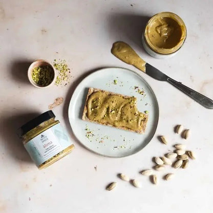 Pistachio tahini spread on toast with a jar of tahini spread and pistachios on a light surface