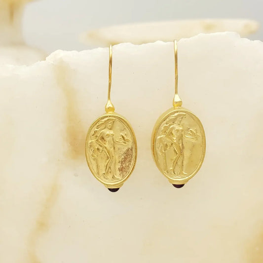 Aphrodite gold oval-shaped earrings hanging on a parchment surface