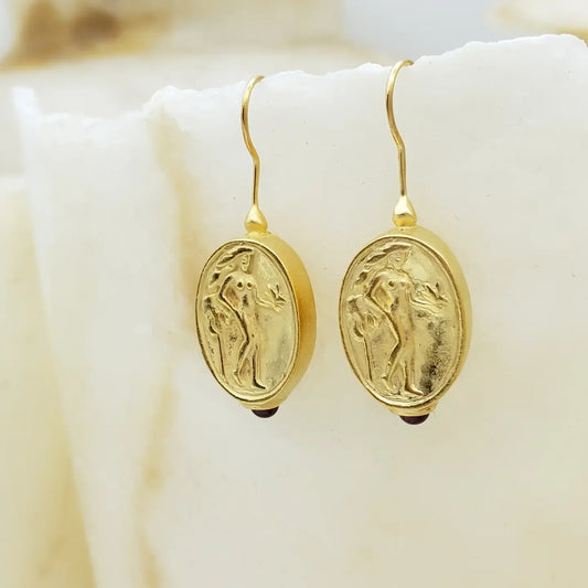 Aphrodite gold earrings with intricate designs hanging to the left on parchment surface
