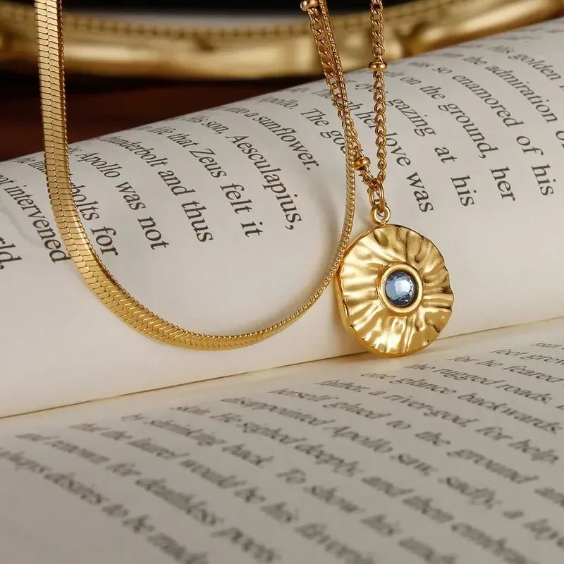 Two layer gold necklace with a blue gemstone pendant on an open book