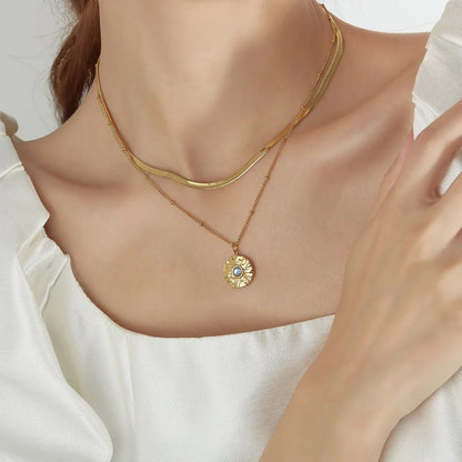 Two layer gold necklace with a blue gemstone pendant on a person wearing a white blouse.