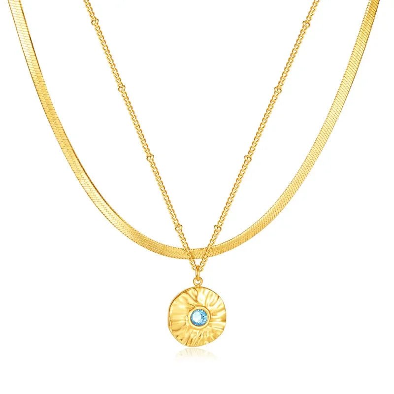 Two layer gold necklace with a round pendant featuring a blue gemstone on a white background
