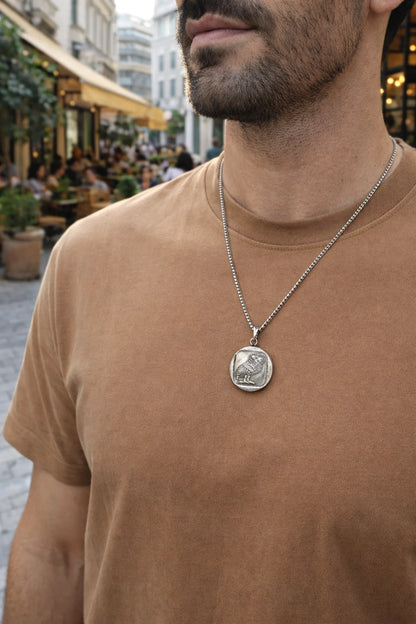 Man wearing a brown t-shirt with a silver necklace featuring a pendant.