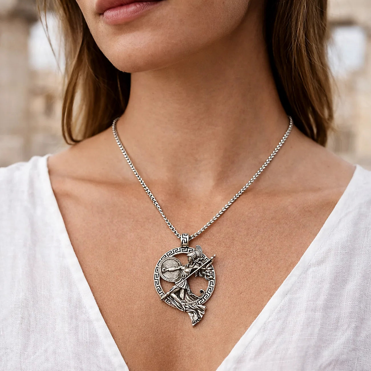 Silver necklace with a detailed pendant worn by a person in a white top.