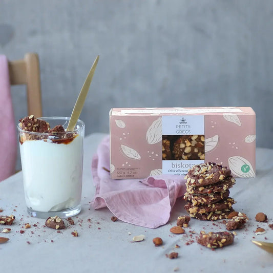 Glass of yogurt with cocoa almond cookies, a pink box of cookies, and cookies on a white surface