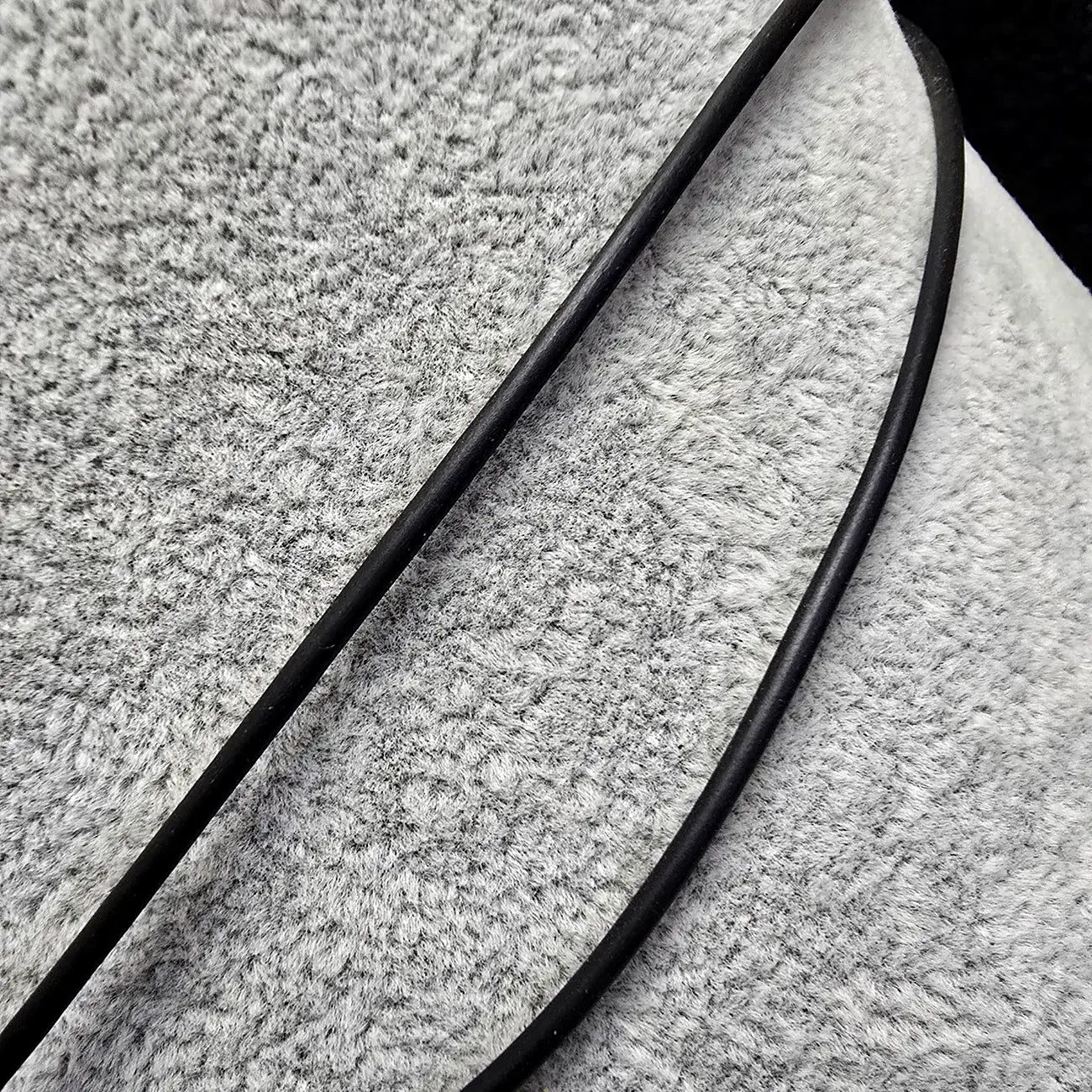 Close-up of textured fabric with a black cords from a necklace running over it