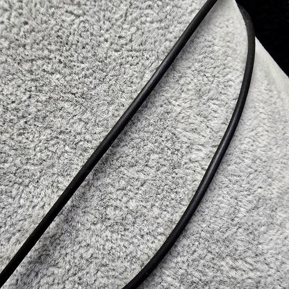 Close-up of textured fabric with a black cords from a necklace running over it