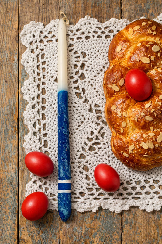 Bread with red eggs and a blue candle on a lace doily over a wooden background