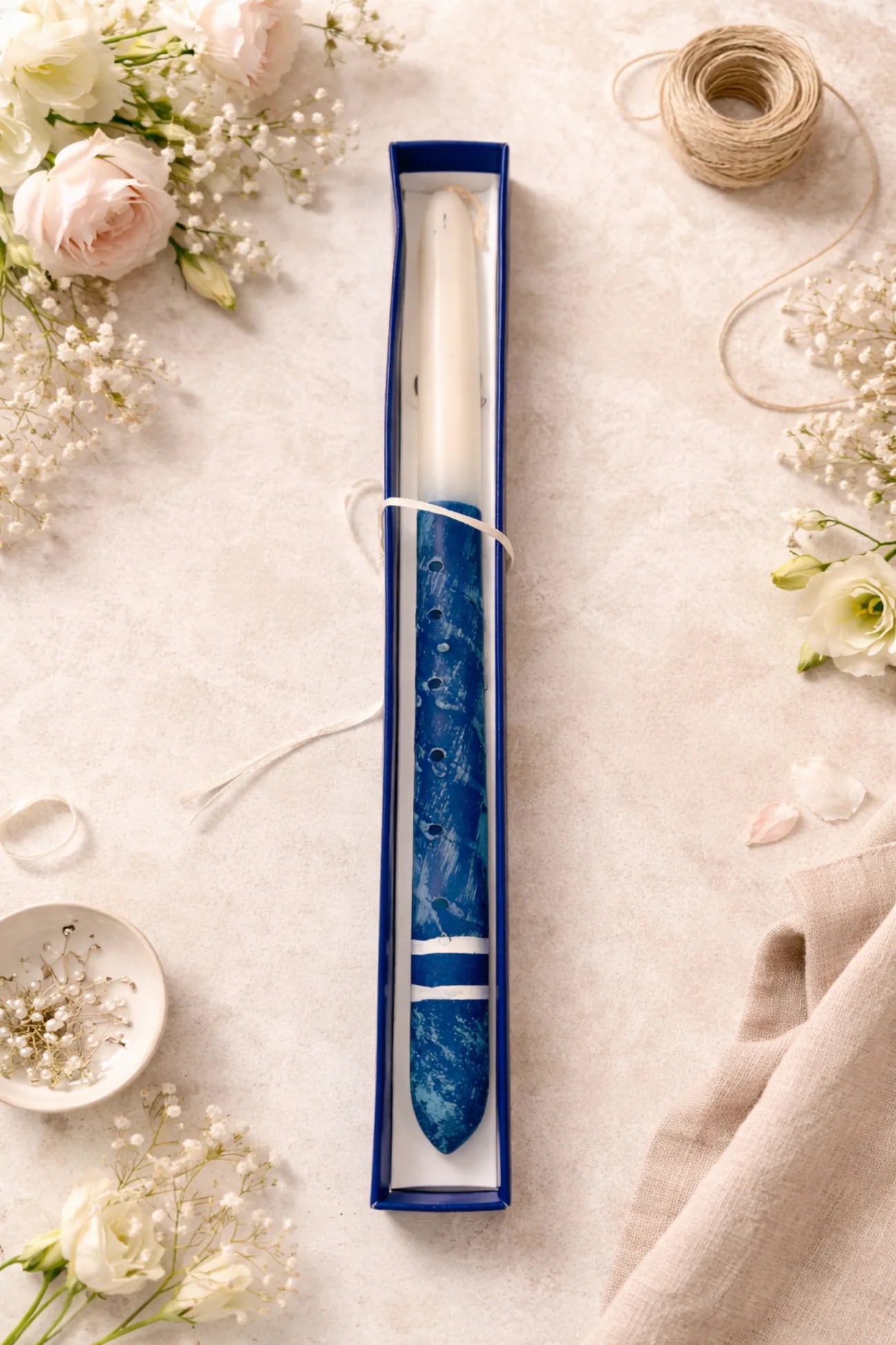 Candle in a blue decorative holder surrounded by flowers on a light surface
