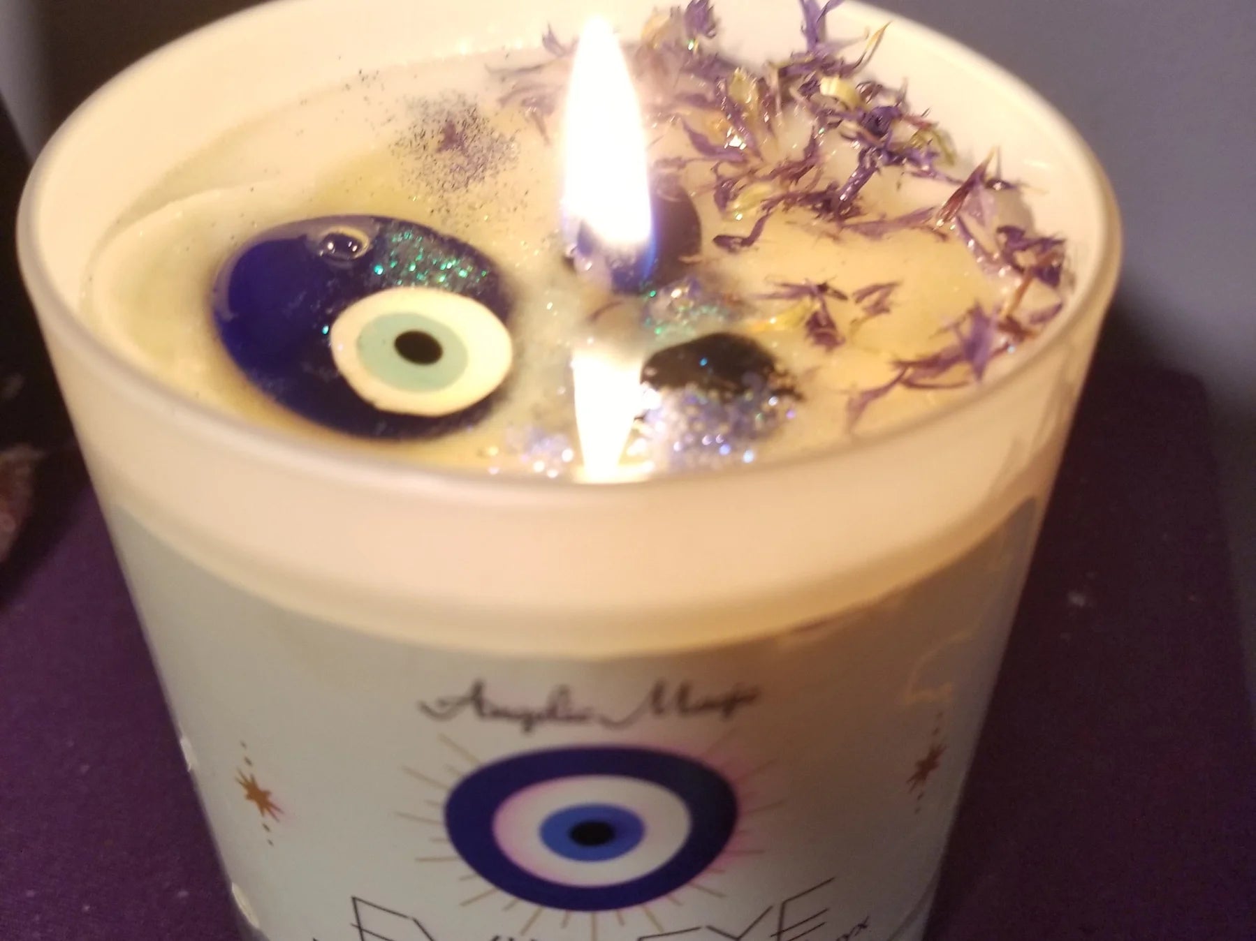 Candle with decorative elements and a visible flame, featuring an eye design